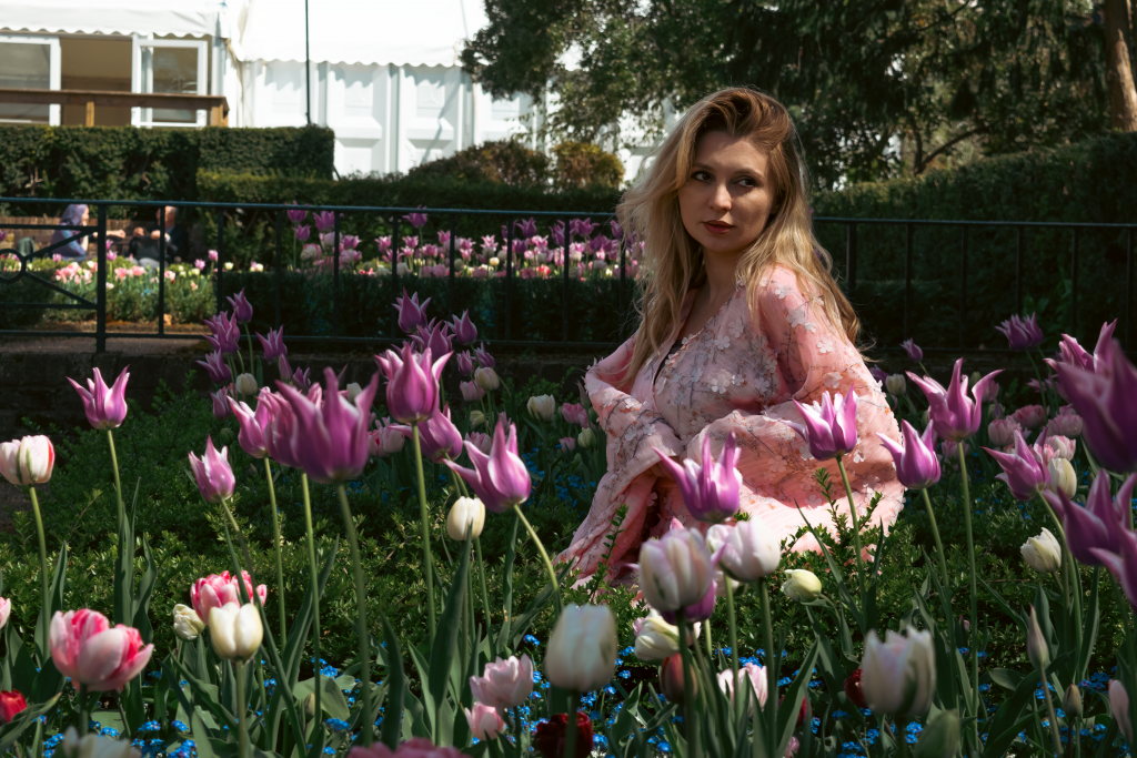 Justyna Sekmistrz sitting in a flowerbed of tulips, wearing a pink kimono and softly lit by dappled sunlight.