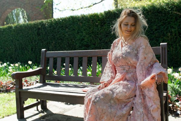 Woman in floral kimono sitting on a bench surrounded by spring flowers.