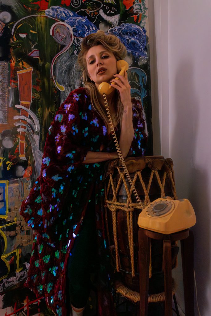 Justyna Sekmistrz poses in a crimson sequin kimono next to a painted wall and vintage phone.